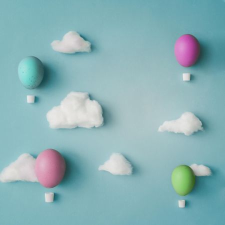 Hot air balloons made of decorated Easter eggs with cotton clouds on bright blue background