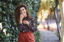 Smiling Arab woman wearing casual clothes in the street lined with greenery