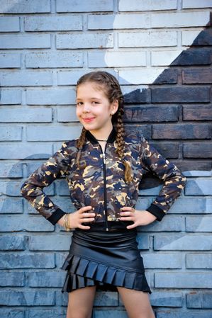 Smiling girl standing and leaning against the wall with both arms akimbo