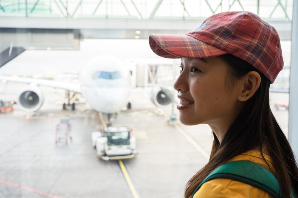 Smiling Asian woman looking down through window at runway with plane