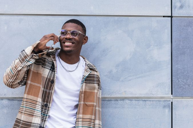 Black man speaking on smartphone near wall