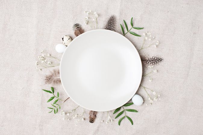 Plate on beige background with leaves, quail eggs and bird feathers