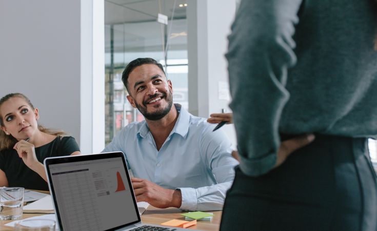 Smiling young man paying attention to female colleague’s presentation in boardroom