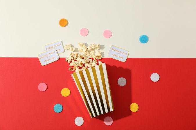 Flat lay. Confetti, tickets and box with popcorn on two tone background
