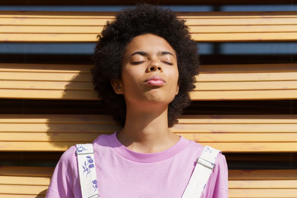Female leaning on wooden shutters in the sun with eyes closed