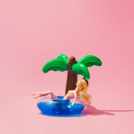 Tropical palm inflatable toy with doll on pink background