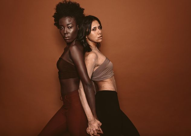 Woman standing with female having vitiligo on brown background