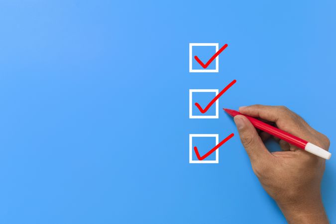 close up of male hand holding red marker and checklist three checkbox isolated on blue background