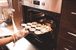 Cropped image of person putting cupcakes in the oven bDJ2K5