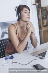Woman sitting at desk with headphones and thinking out problem 4B3BBb