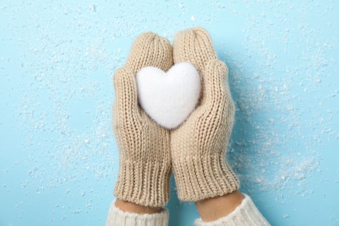 Girl holding in hands heart on blue background with snow, space for text