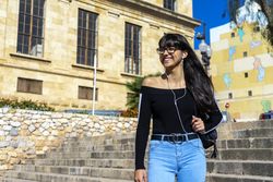 Young smiling woman wearing earphones spending free time outdoors in the sun
