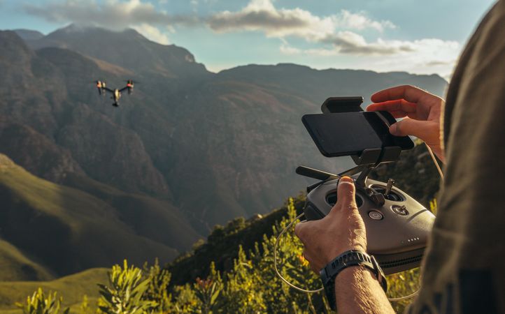 Close up of man flying a drone in green mountains and taking pictures