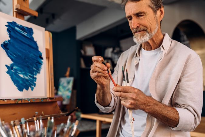 Bearded artist flicking brush in front of easel