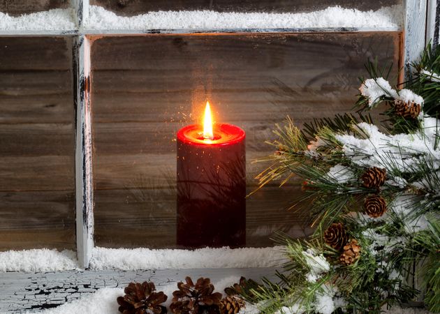 Christmas red candle with snow covered home window and pine tree branch
