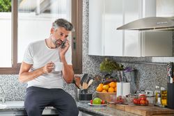 Man talking on cellphone and drinking coffee in kitc