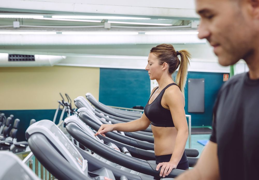 Side view of male and female on row of gym treadmills