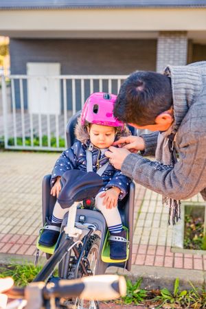 Portrait of father securing helmet on daughter in bike seat