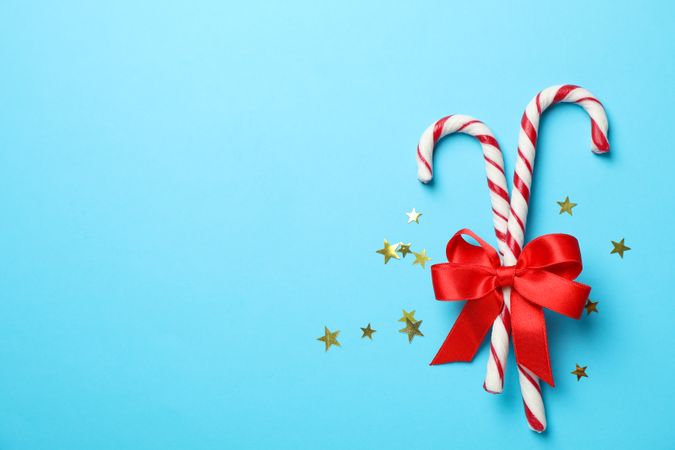 Sweet candy canes and bow on color background, space for text