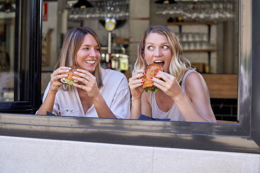 Happy women eating burgers together in cafe
