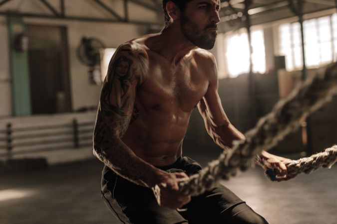 Powerful man exercising with battle ropes at gym