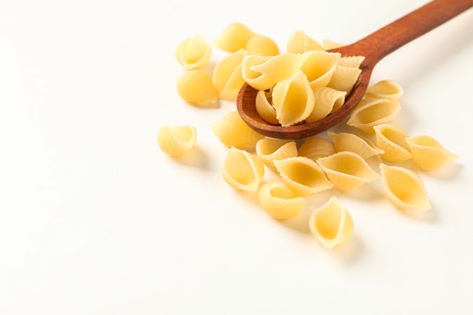 Wooden spoon with pasta on blank background, space for text. Dry uncooked whole pasta