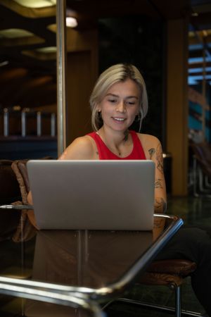 Smiling young woman in red tank top working on laptop computer in a coffee shop