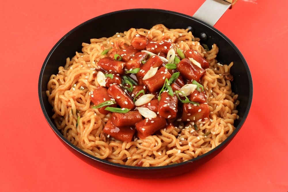 Pan of noodles topped with Korean rice cakes with red background
