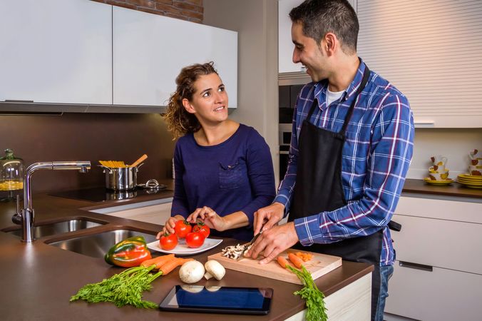 Portrait of couple smiling as they cut vegetables for dinner