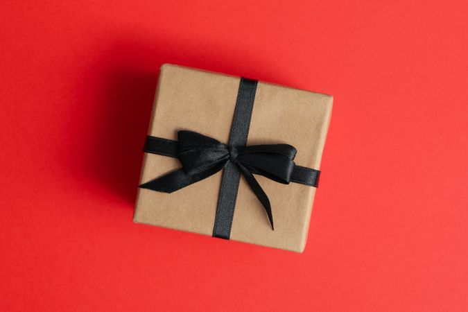 Gift box with dark bow on red background