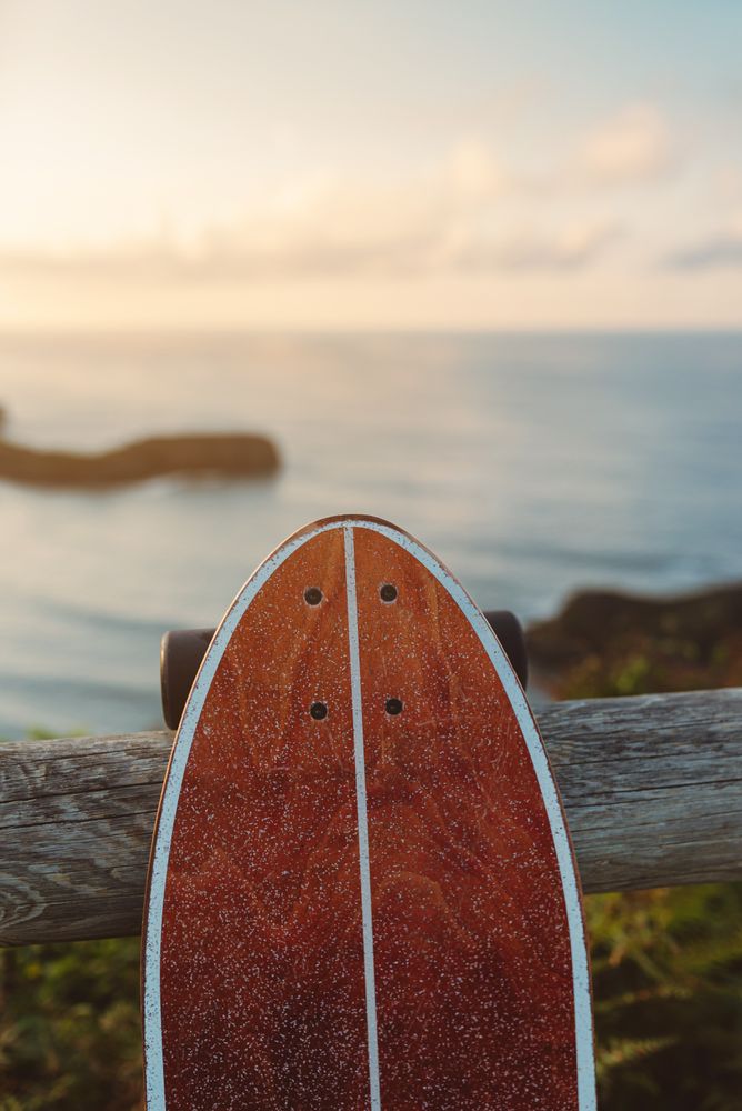 Surf skate leaning on wooden railing against blurred beach