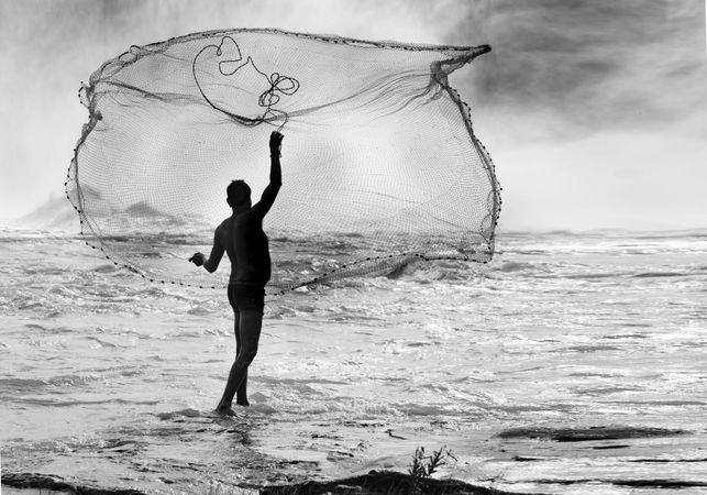 Back view of topless fisherman throwing fishnet to the sea in grayscale