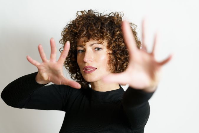 Woman in dark sweater looking through two hands with palms to the camera