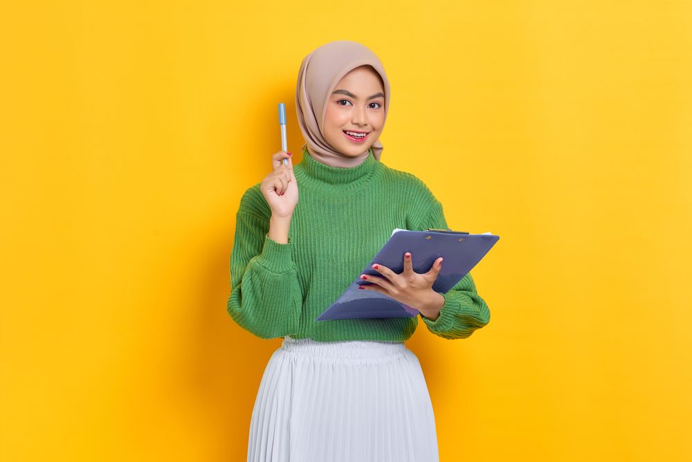 Surprised woman in headscarf holding up pen and holding clipboard