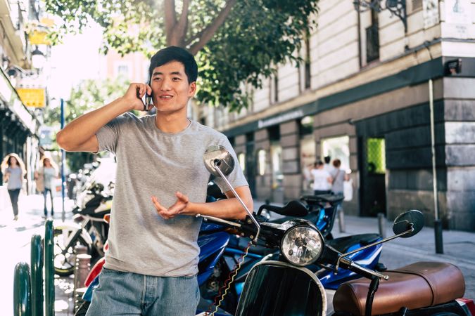 Confident Asian man talking on phone while standing by motorbike
