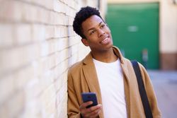 Curious Cuban male leaning against wall holding his phone
