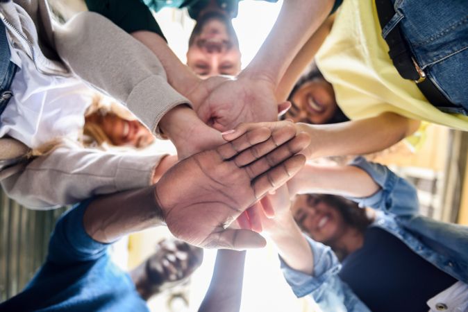 Group of friends putting their hands together in circle, view from bottom up