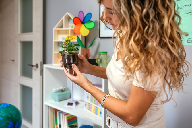 Woman holding a pansy plant inside of glass pot in ecology classroom