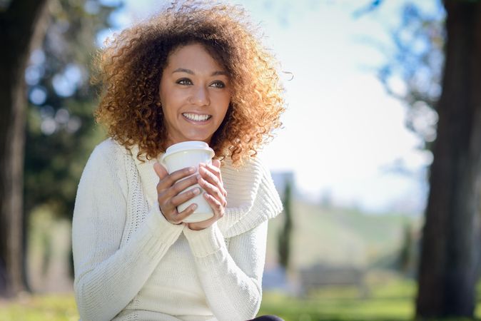Smiling Black woman sipping coffee from to go drink outside