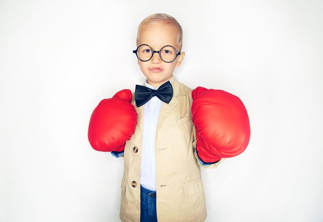 Blond boy wearing round glasses with red boxing gloves raised