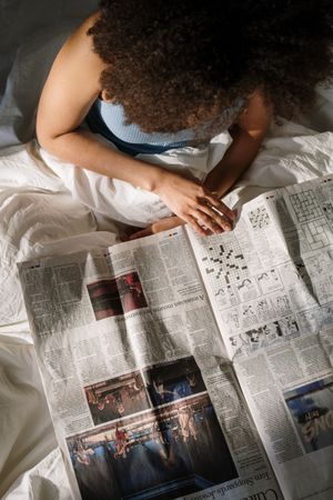 Top view of woman with curly hair reading newspaper