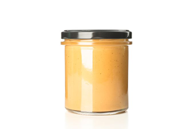 Creamy peanut butter in glass jar isolated on bright background. A traditional product of American cuisine