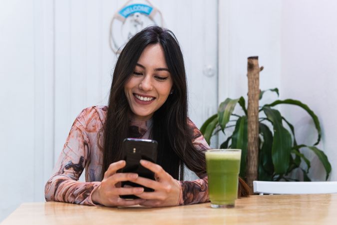 Smiling woman using smartphone at table in bar