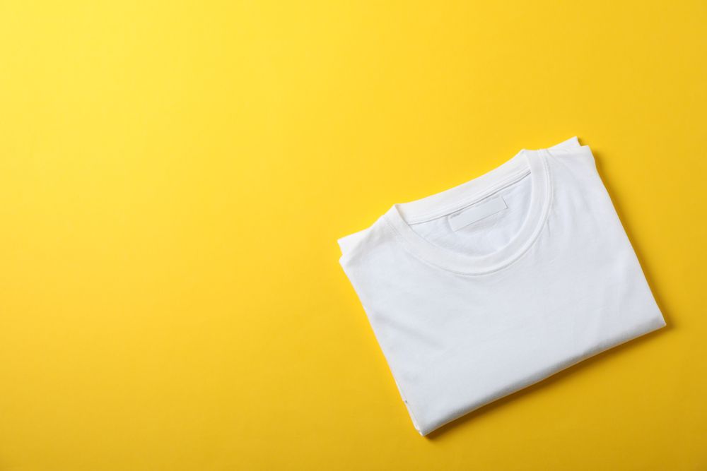 Folded blank plain t-shirt on yellow background, space for text