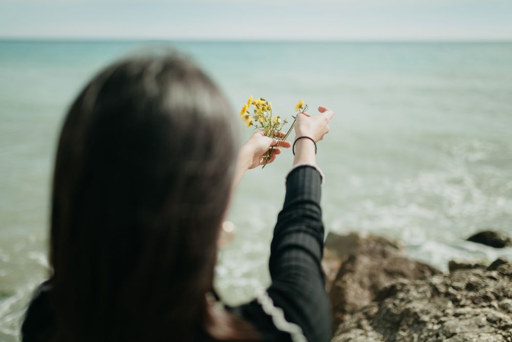 Anonymous woman throwing flowers in sea