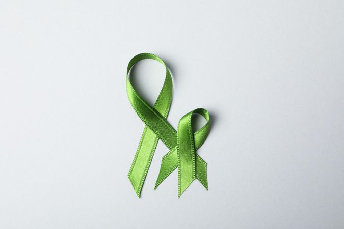 Green awareness ribbons on grey background, space for text