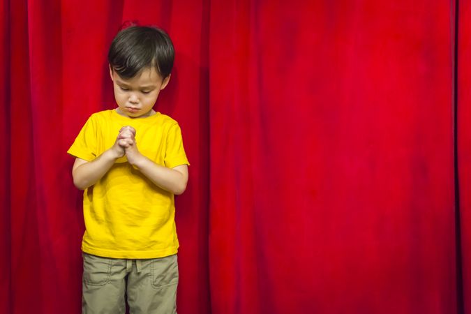 Biracial Boy Praying in Front of Red Curtain