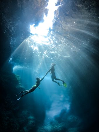 Underwater shot of man and woman diving in water and holding hands