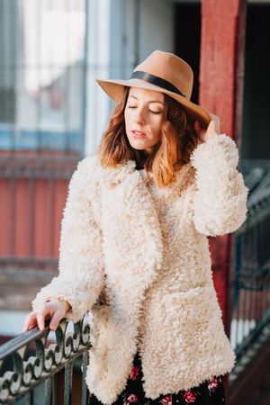 Smiling woman in warm wear standing near building and fence