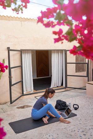 Woman with laptop on yoga mat in house yard